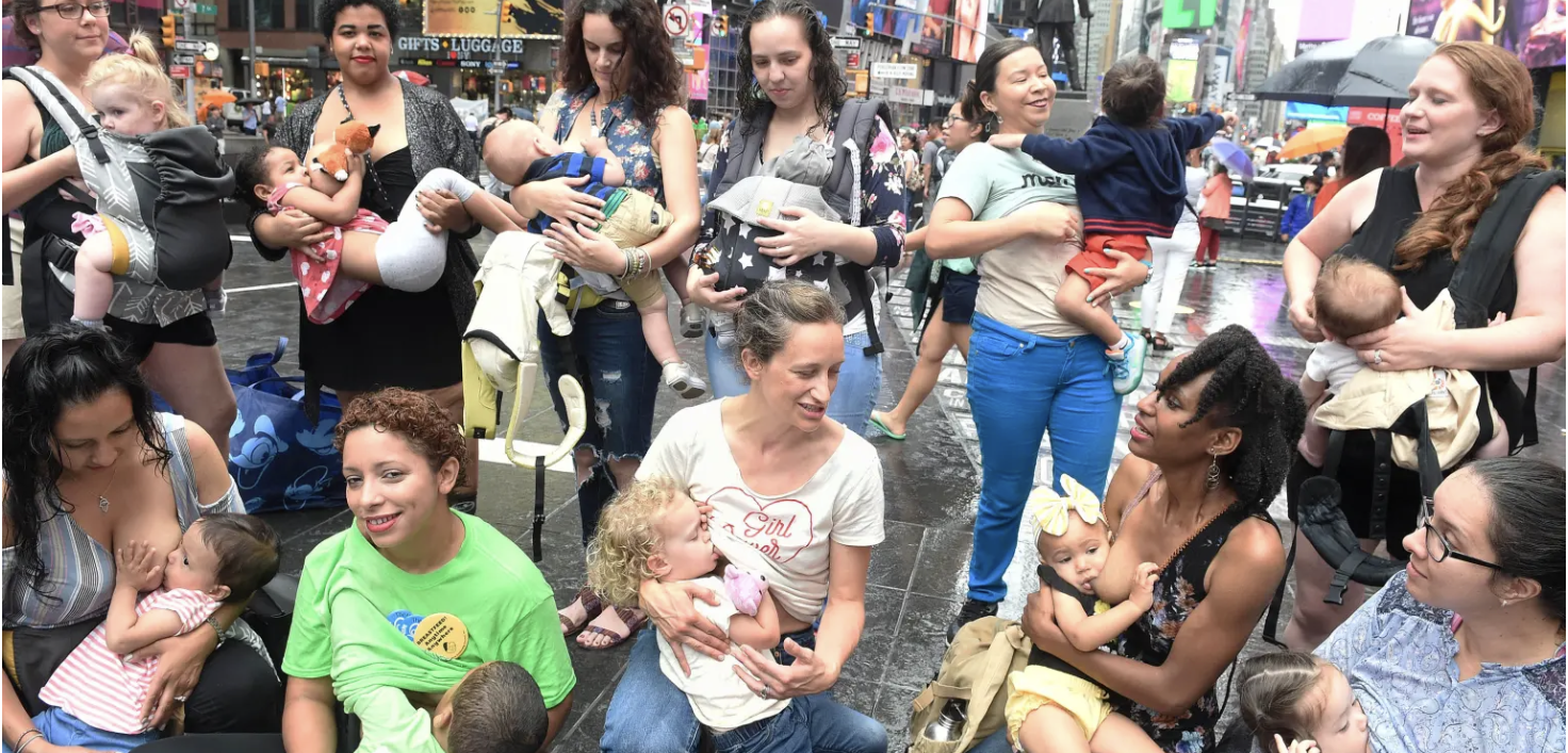 A group of women sit together with their babies latched to their breasts